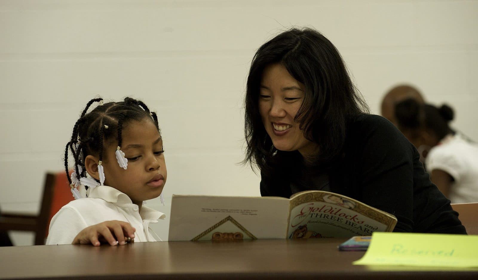 A tutor and a young student reading a picture book together at a table