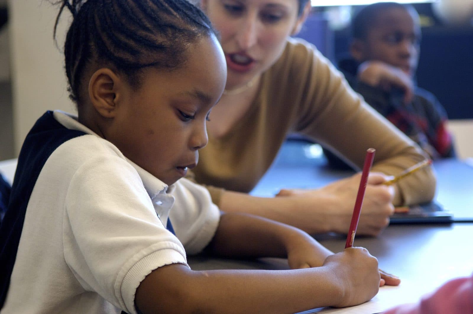 A young student writing carefully while a tutor watches